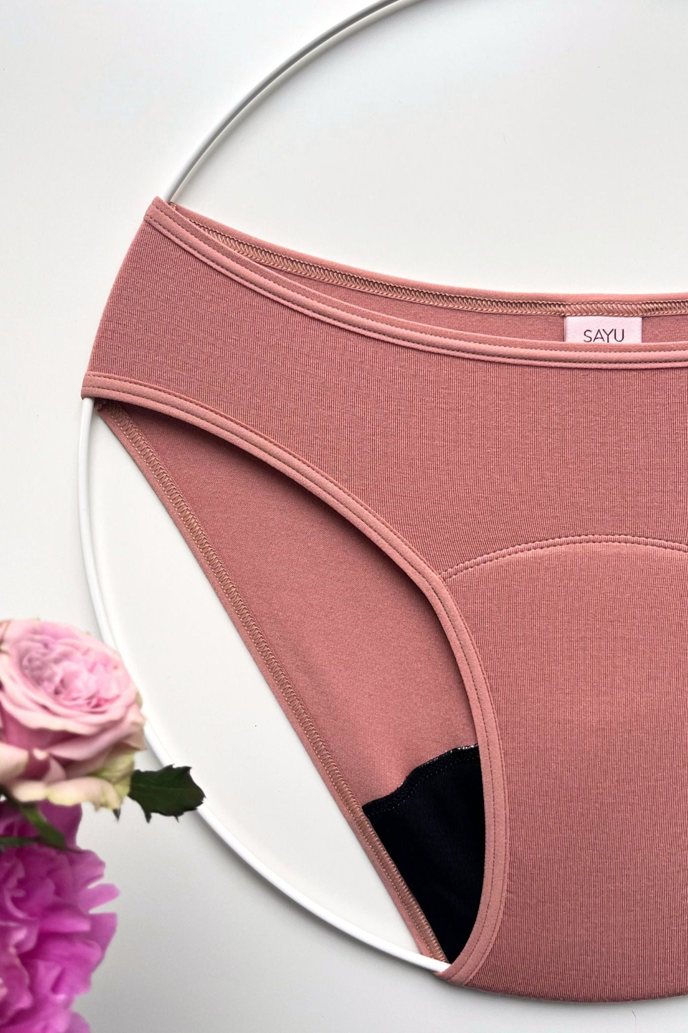 Menstruační SAYU kalhotky klasického střihu v barvě růžové latte, foceno na bílém pozadí s květinami