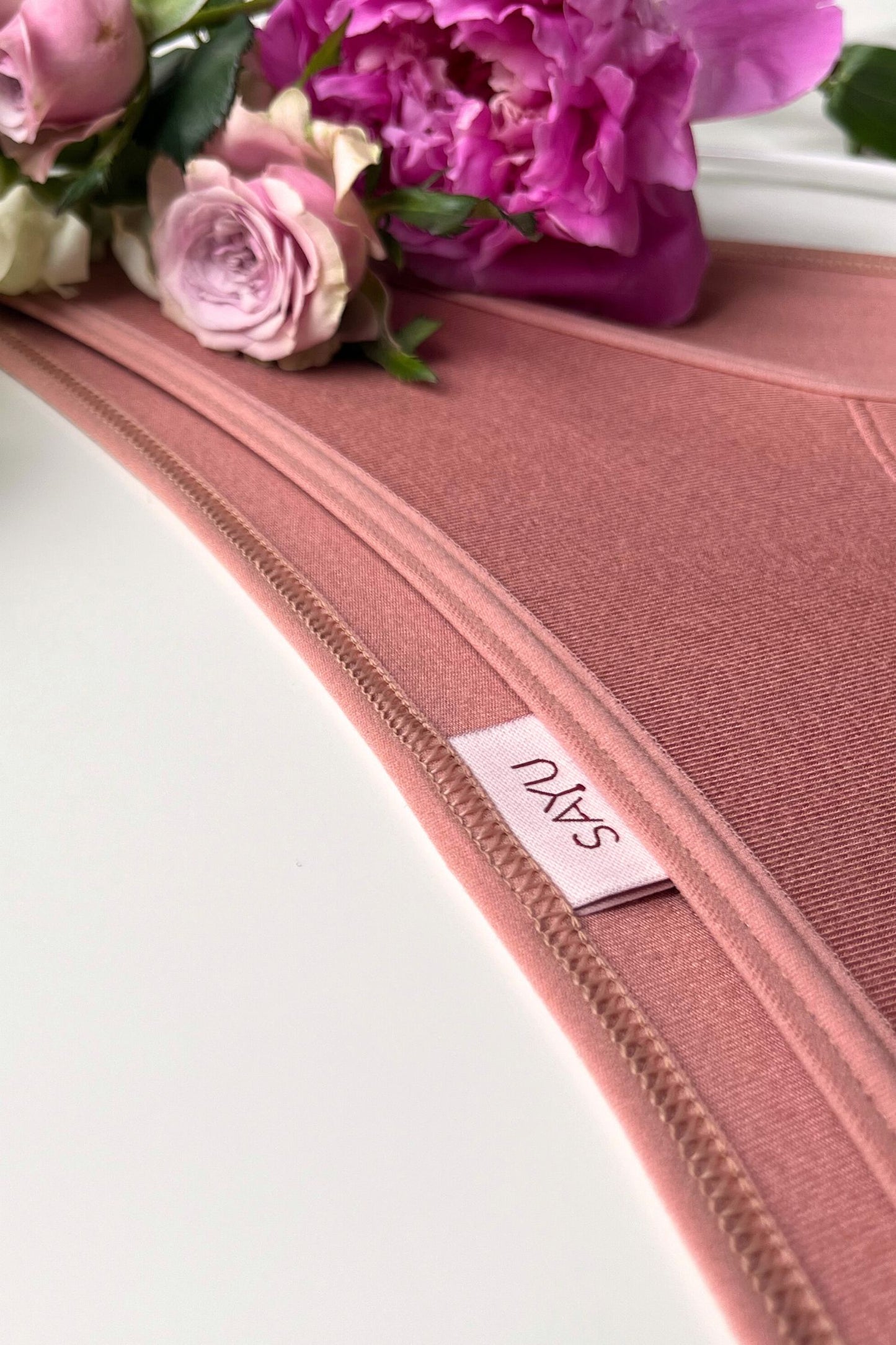 Detail na švy a etiketu menstruačních SAYU kalhotek klasického střihu v barvě růžové latte, foceno na bílém pozadí s květinami