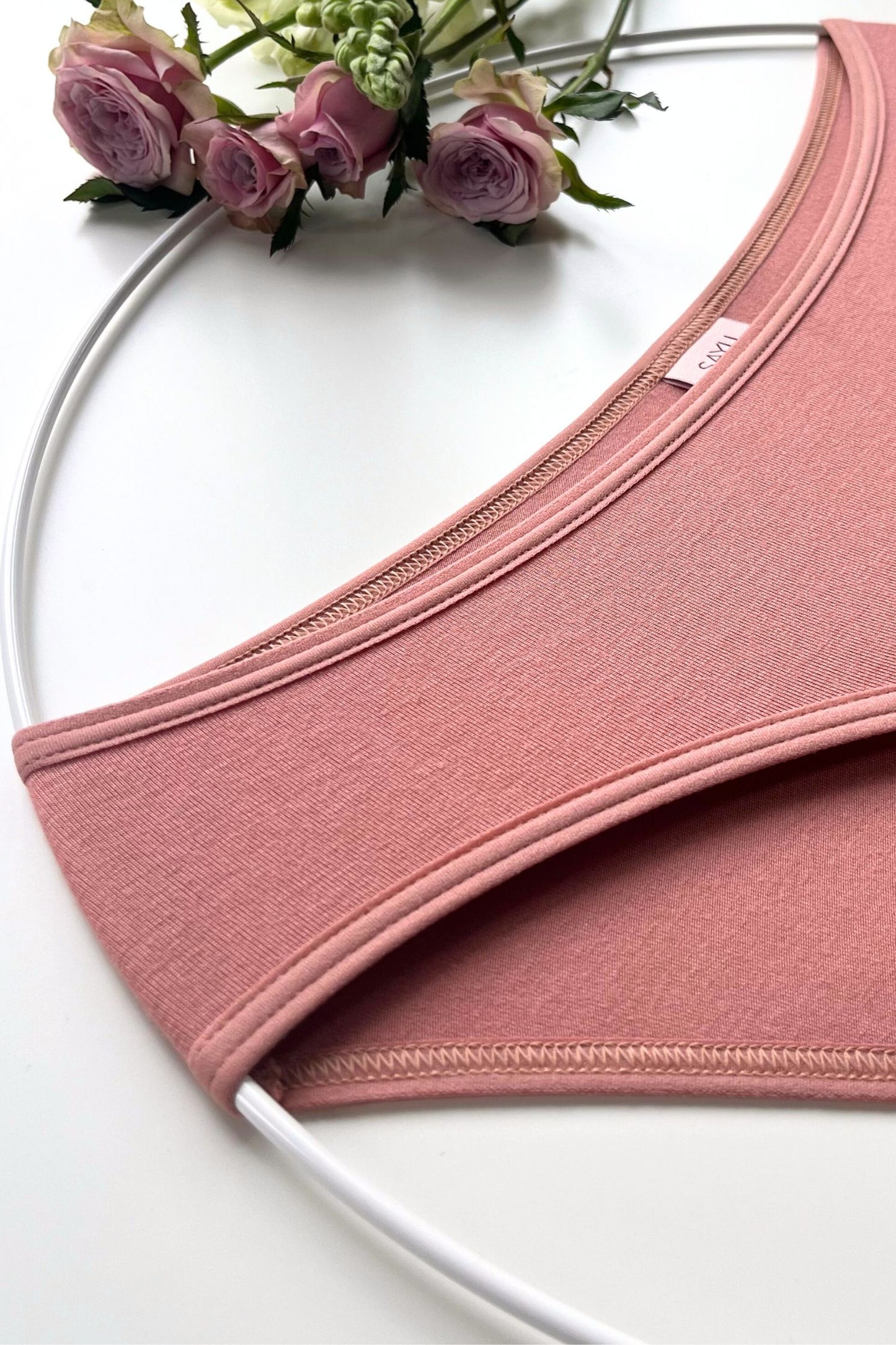 Detail na švy růžových menstruačních kalhotek SAYU s merino dotykovou funkční vrstvou, foceno na bílém pozadí s květinami