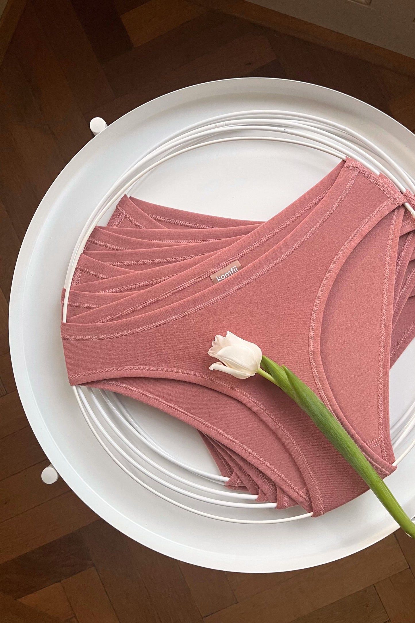 pohled na set 5ti nemenstruační kalhotkek komfii bikini briefs v barvě růžové latté na kruhu položené na stolku s tulipánem