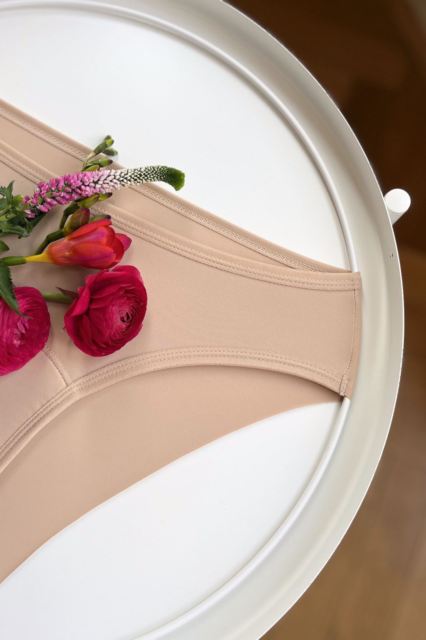 Detailní pohled na boční šev a zadní řezaný okraj menstruačních brazilek neviditelných pod oblečením.