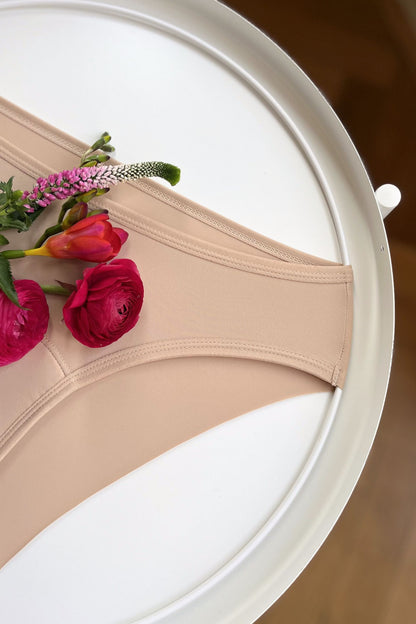 Detailní pohled na boční šev a zadní řezaný okraj menstruačních brazilek neviditelných pod oblečením.