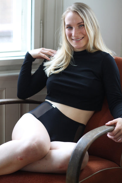Pasové černé menstruační kalhotky s transparentními boky na sedící modelce