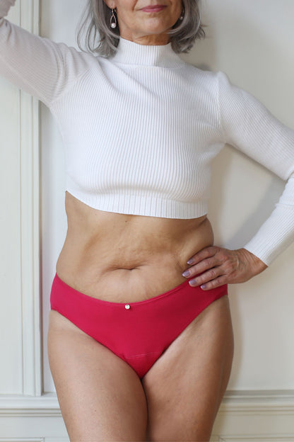 přední pohled na modelku, která má ruku v bok a na sobě menstruační kalhotky klasického střihu ve svěže růžové barvě