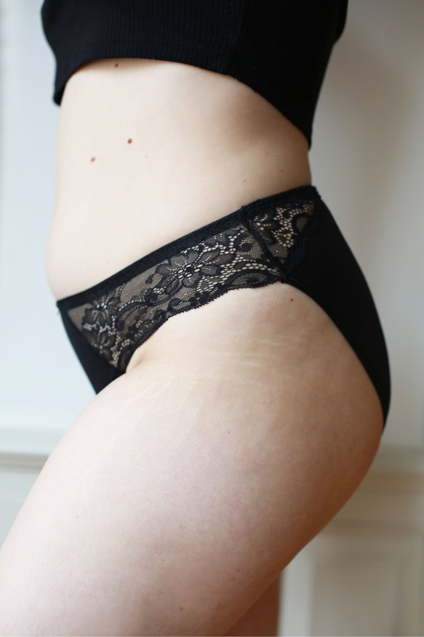 Boční pohled na krajku rafinovaných menstruačních kalhotek klasického střihu v černé barvě a střední absorpci.