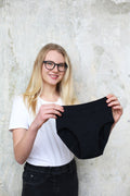 Modelka drží v rukou černé menstruační kalhotky v dívčí velikosti.